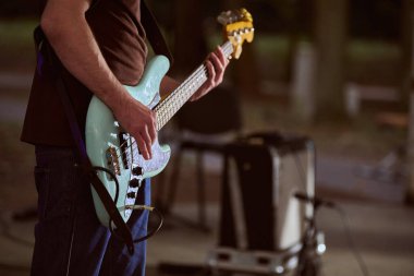 Kaliningrad, Rusya - 11.08.2024 - Yetişkin erkek parkta turkuaz gitar çalıyor. Rahatlamış atmosfer, akşam ışığı, doğa arka planı sahneyi büyütüyor