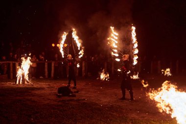 Kaliningrad, Rusya - 10.09.2022 - İki kadın ateş gösterisi sanatçısı koyu arka plana karşı alevli ateş kanatları ile, canlı performans yoğunluğu ve heyecanı yakalıyor