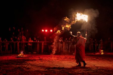Kaliningrad, Rusya - 10.09.2022 - Tanrı 'nın tarihi kostümlü ateş sanatçısı seyircilerin önünde ateşli asasını sallıyor, dramatik kırmızı ışık çarpıcı, dünyevi bir parıltı yaratıyor