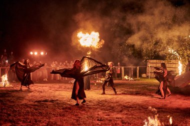 Kaliningrad, Rusya - 10.09.2022 - Muhteşem gece gösterisinde otantik bir elbiseyle dans eden ateş gösterisi sanatçıları, gece gökyüzü altında ateşli hareketler, izleyiciler
