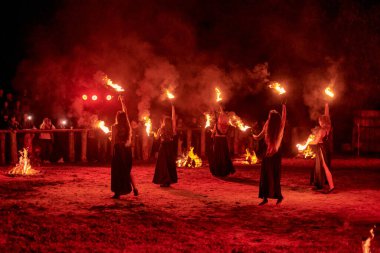 Kaliningrad, Rusya - 10.09.2022 - Muhteşem gece gösterisinde otantik bir elbiseyle dans eden ateş gösterisi sanatçıları, gece gökyüzü altında ateşli hareketler, izleyiciler