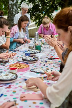 Kaliningrad, Rusya - 10.08.2024 - Canlı açık hava atölyesinde mozaik sanat eserleri yapan çeşitli yetişkinler grubu. Parlak, doğal ışık yaratıcılığı ve odaklanmayı arttırır.