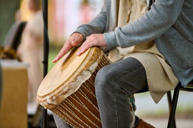 Kaliningrad, Rusya - 10.08.2024 - parkta djembe oynayan genç bir adam. Günlük kıyafetler, rahat bir hava. Doğal ışık, arka plandaki yeşillik sahneyi güçlendirir