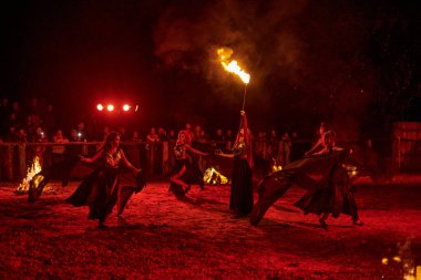 Kaliningrad, Rusya - 10.09.2022 - Muhteşem gece gösterisinde otantik bir elbiseyle dans eden ateş gösterisi sanatçıları, gece gökyüzü altında ateşli hareketler, izleyiciler