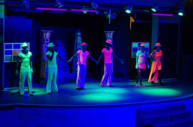 Sharm el Sheikh, Mısır - 13.08.2014 - Neon kostümlü genç yetişkinler, mavi ışıklar altında parlıyorlar. Koyu arkaplana karşı canlı renklerle enerjik dans