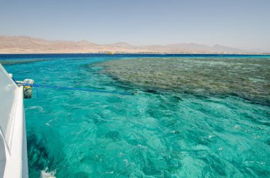 Kristal berrak turkuaz su ve mercan resifi parlak gökyüzünün altında uzanıyor. Uzak dağlardan, sakin deniz manzarasını güzelleştiren bir tekneden bakıyorum. Güneş ışığı dalgalar üzerinde parıldıyor