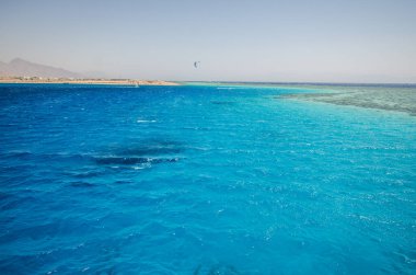 Kızıl Deniz 'in berrak gökyüzünün altında canlı turkuaz suları gösteren hava manzarası. Sakin dalgalar ince desenler oluşturur, uzak ufuklarla buluşur.