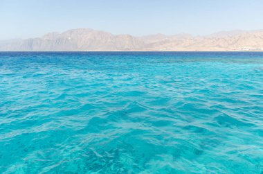 Kızıl Deniz 'in turkuaz dalgaları gün ışığında parıldıyor ufukta kurak dağlarla karşılaşıyor. Serene ayarı, deniz seviyesi perspektifinden görülen canlı paletleri yakalar