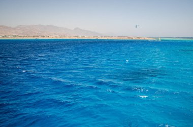 Kızıl Deniz 'in berrak gökyüzünün altında canlı turkuaz suları gösteren hava manzarası. Sakin dalgalar ince desenler oluşturur, uzak ufuklarla buluşur.