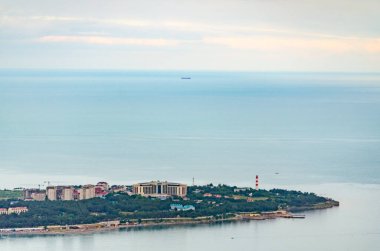Gelendzhik, Rusya 'nın hava görüntüleri, kıyı binaları ve yemyeşil alanlar. Sakin deniz, yumuşak, bulutlu ışık altında ufka doğru uzanıyor. Baskın soluk maviler ve yeşiller rahatlatıcı bir sahne yaratır