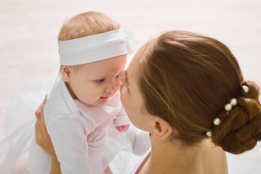 Kahverengi saçlı beyaz kadın balerin gülümseyen bir kız bebek. Yumuşak ışıklı bale stüdyosunda, her ikisi de beyaz dans kıyafeti giyerler. Bağlanma, huzur ve neşe