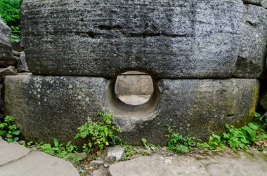 Büyük taş dolmende dairesel bir açıklık var. Yeşillik bir alanda, hava durumu belirtileri gösteriyor. Yapı gizemli ve eski bir atmosfer yaratır.