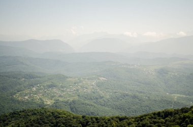 Havadan bakıldığında geniş yeşil dağların etrafa dağıldığını görüyoruz. Yumuşak güneş ışığı, uzaktan gelen sisli tepelerle harmanlanan hafif bir parıltı yayar. Sakin ve huzurlu atmosfer hüküm sürüyor.