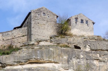 Kırım uçurumunun tepesinde, gökyüzü arkaplanı açık taş kale harabeleri var. Güneşli sahne, engebeli mimari ve yıpranmış taşı ön plana çıkarıyor. Nadir bitki örtüsü kırsal cazibe ekler.