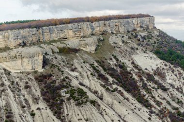 Bulutlu gökyüzünün altındaki suç tebeşirli uçurumların geniş bir manzarası engebeli araziyi ve sessiz renkleri vurguluyor. Bitki örtüsü araziyi az noktalar. Hava perspektifi dramatik jeolojik oluşumları vurguluyor