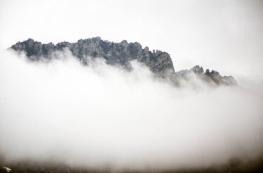Kırım 'da engebeli dağ zirveleri yoğun sislerin arasından çıkar. Yumuşak sabah ışığı manzarayı aydınlatır, gizemli atmosferi güçlendirir. Durgun tonlar dinginliği ve ruhani manzarayı güçlendirir