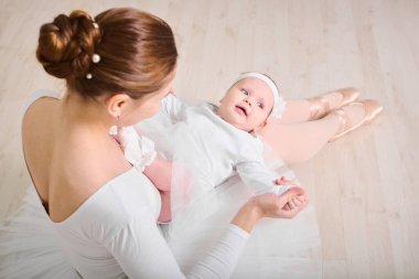 Genç bayan balerin küçük kızı ahşap zeminde beşikte tutuyor. Işık tonları sıcak ve sakin bir atmosfer yaratır. Anneler neşeli, bağlanan anın altını çiziyor