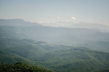 Expansive mountain range extends under delicate haze. Rolling peaks create serene landscape with lush greenery. Gentle light bathes scene, enhancing peaceful atmosphere clipart