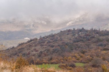 Huzurlu Kırım manzarası sisle kaplanmış yuvarlanan tepeleri yansıtıyor. Sonbahar renkleri hakim, bulutlu gökyüzü sakin atmosferi arttırıyor. Yumuşak yamaçlar ve bitki örtüsü cennet gibi bir ortam yaratır.