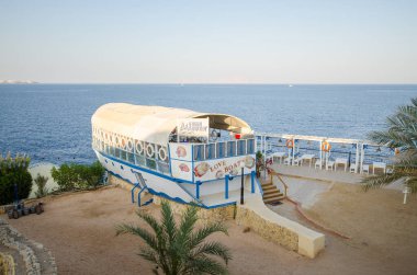 Resort with boat-shaped restaurant offering stunning ocean views. Palm trees frame sandy foreground. Soft, natural lighting enhances tranquil ambiance clipart