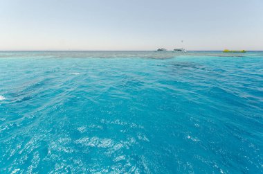 Kızıl Denizler 'in turkuaz sularının parlak gündüz manzarası. Geniş gökyüzü ve uzak ufuk huzurlu atmosferi güçlendirir. Canlı renkler zarif deniz ortamını vurgular