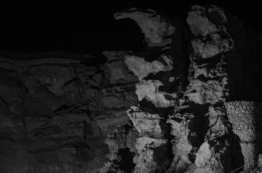 Dramatic night lighting highlights rugged cliff in resort. Shadows play across rocky surface, creating natural art piece. Dark sky enhances mysterious atmosphere clipart