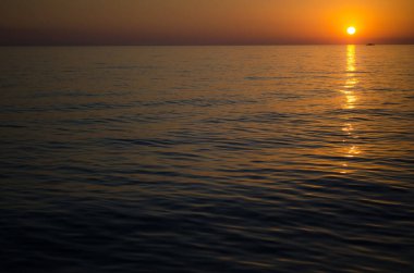 Güneş engin okyanusun üzerinde batar, sakin sulara altın yansımalar yapar. Horizon sıcak tonlu gökyüzüne karışıp sakin ve sakin bir manzara yaratıyor. Düşük açı perspektifi derinliği ve güzelliği arttırır