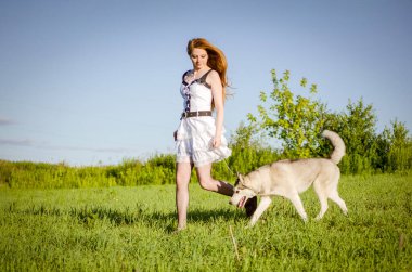 Uzun kızıl saçlı, beyaz elbiseli, köpeğini güneşli çayırlarda gezdiren genç bir kadın. Ayaklarının altında yeşil çimenler, tepemizde açık mavi gökyüzü. Sakin atmosfer, doğal güzellik