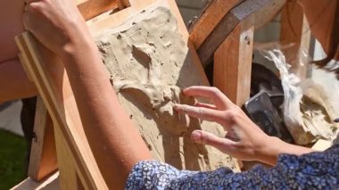 Yaratıcı açık havada eller güneşin altında kil kabartmasını şekillendirir. Tahta tahtada sanat eserleri var. Doğal ışıklandırma dokuyu ve detayı geliştirir