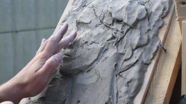 Eller kil kabartması üzerine karmaşık desenler yontuyor. Tarafsız tonlar kompozisyona hakim. Dokulu arka plan derinlik katıyor. Açı işçiliği ve dikkati vurgular