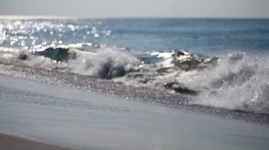 Sakin dalgalar, parlak güneş ışığı altında yumuşak kumlu plajda tur atar. Horizon berrak mavi gökyüzü ile buluşup sakin bir kıyı manzarası yaratıyor. Işıl ışıl suyla yumuşak bir ortam.