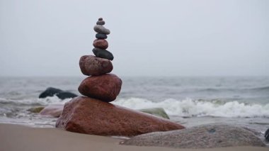 Sakin denize karşı kumlu sahilde dengelenmiş taşlar kulesi. Bulutlu gökyüzü sükuneti artırır, meditasyon atmosferini güçlendirir. Topraksı tonlar sakin kıyı ortamını tamamlar