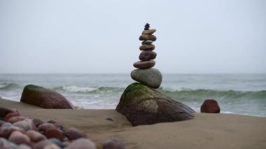 Okyanus dalgalarının yanındaki kumlu sahilde uzun taş yığını duruyor. Bulutlu gökyüzü dingin bir atmosfer yaratarak yeryüzünün tonlarını arttırır. Düşük açı dengeyi ve hassasiyeti yakalar.