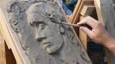 El ustalıkla kil kabartmasını ahşap destekle şekillendirir, yumuşak gün ışığında hassas özellikleri yakalar. Tarafsız tonlar, karmaşık işçiliğe odaklanmayı artırır