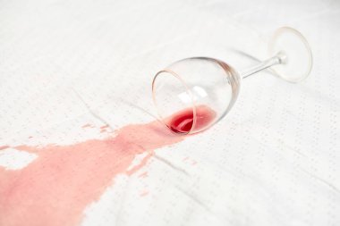 Tepetaklak şarap kadehleri beyaz masa örtüsünün üzerinde, kırmızı şarap ise canlı bir leke bırakıyor. Parlak ışıklandırma kumaşa karşı sıvı kontrastı vurgular. Sahne istem dışı kazayı yakalar