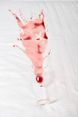 Kırmızı şarap beyaz kumaşa yayılır ve soyut desenler yaratır. Camlar lekenin yanına eğilmiş, son dökülmeye işaret ediyor. Işık kırmızı ve beyaz arasındaki karşıtlığı artırır