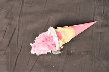 Paketlenmemiş pembe dondurma külahı erimiş içerikli koyu gri yüzeyde uzanıyor. Yumuşak ışıklandırma dondurmanın dokulu görünümünü artırarak, arka planda tam bir karşıtlık yaratır