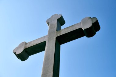 Büyük taş haç, parlak mavi gökyüzüne ayarlanmış, alçak açıdan çekilmiş. Güçlü şekiller ve açık gri renkler canlı arkaplanlı. Resim dinginliği ve gücü iletir
