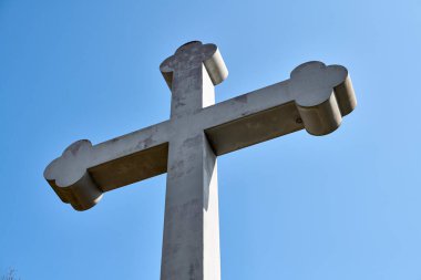 Büyük taş haç, parlak mavi gökyüzüne ayarlanmış, alçak açıdan çekilmiş. Güçlü şekiller ve açık gri renkler canlı arkaplanlı. Resim dinginliği ve gücü iletir