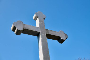 Büyük taş haç, parlak mavi gökyüzüne ayarlanmış, alçak açıdan çekilmiş. Güçlü şekiller ve açık gri renkler canlı arkaplanlı. Resim dinginliği ve gücü iletir