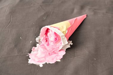 Paketlenmemiş pembe dondurma külahı erimiş içerikli koyu gri yüzeyde uzanıyor. Yumuşak ışıklandırma dondurmanın dokulu görünümünü artırarak, arka planda tam bir karşıtlık yaratır