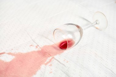 Tepetaklak şarap kadehleri beyaz masa örtüsünün üzerinde, kırmızı şarap ise canlı bir leke bırakıyor. Parlak ışıklandırma kumaşa karşı sıvı kontrastı vurgular. Sahne istem dışı kazayı yakalar