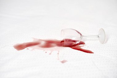 Şarap kadehi devrildi ve kırmızı şarap beyaz masa örtüsüne döküldü. Leke kontrastı çarpıcı bir görsel yaratıyor, kaosu vurguluyor. Parlak ışıklandırma kırmızı ve beyaz karşıtlığı vurgular