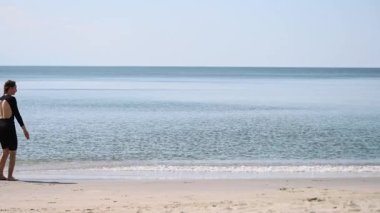 Kahverengi saçlı genç bir kadın, Baltık Denizi kıyısında kumlu sahilde takla atıyor. Açık mavi gökyüzü ve sakin sular dingin bir zemin oluşturur. Hareketin ortasında yakalanan enerjik, neşeli atmosfer