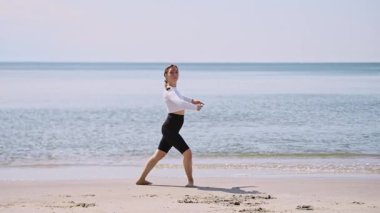 Genç bayan, koyu saçlı balerin kumsalda zarifçe gösteri yapıyor. Baltık Denizi parlak güneşin altında arka planda parlıyor. Huzur ve zarafet çok güzel yansıtılıyor.