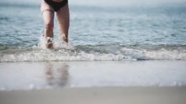 Baltık kıyısı boyunca koşan genç yetişkin bacakları hareket halinde bulanıktı. Parlak yaz güneşi, dingin ufukta dalgaları yansıtır. Sandy önplanı dinamik sahneye doku ekler