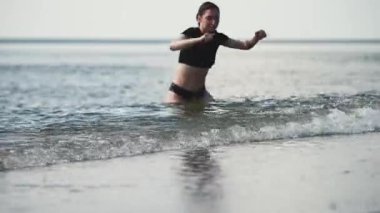 Siyah saçlı genç bir kadın Baltık deniz sahilinde koşuyor. Güneş ışığı dalgaları bacaklarının etrafına vuruyor. Neşeli yaz atmosferi, serin deniz esintisi