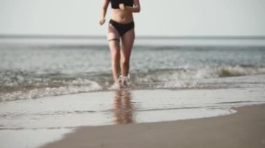 Açık tenli genç bir kadın, kumlu deniz sahillerinde yürüyor. Yumuşak dalgalar kıyıya vurur berrak, parlak gökyüzünün altında. Huzurlu yaz atmosferi ve sakin deniz manzarası