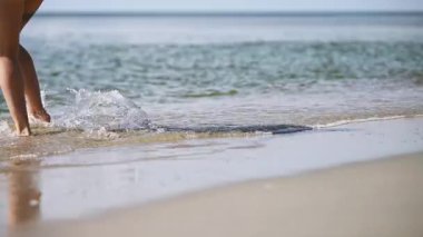 Güneşli sahilde yürüyen kadın bacakları, hafif baltık deniz dalgaları. Kıtır, berrak gökyüzü ve sakin su huzurlu, yaz havası yaratır. Perspektifi kapat hareketi yakalar