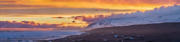 アイスランドの海岸に氷が浮かぶ黒い砂の上に男の姿をした素晴らしい夕日の空 — ストック写真
